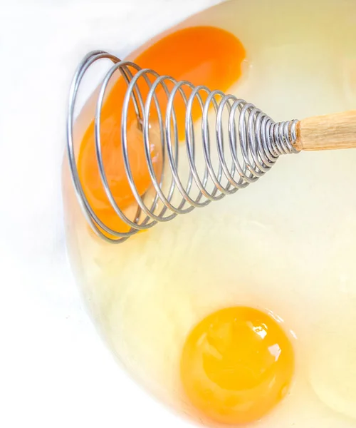 stock image spiral culinary whisk for whipping with wooden handle in a white bowl with broken chicken eggs. 