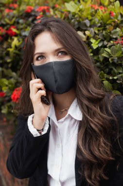 Çiçeklerin önünde oturan iş kadını cep telefonundan arıyor.