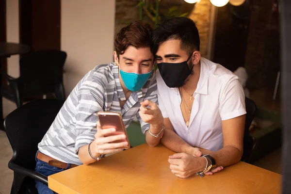 gay couple wearing mouth covers while using their cell phone in a restaurant covid 19