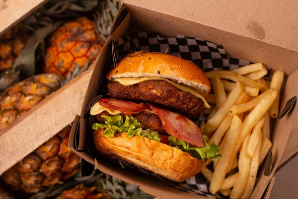 arka plan ananasları, çift etli burger ve paketinde patates kızartması.