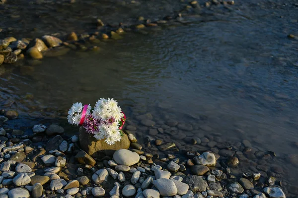 Flowers by the river, a bouquet of flowers on a stone seashore, a bouquet of flowers in the water, sunset photo of a bouquet in water — Stock Photo, Image