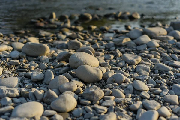 Pietre enormi sulla riva del fiume. Pietre del fiume e acqua pulita e limpida del fiume. Pietre di ghiaia sulla riva sono vicino alla luce del tramonto offuscata sullo sfondo. — Foto Stock