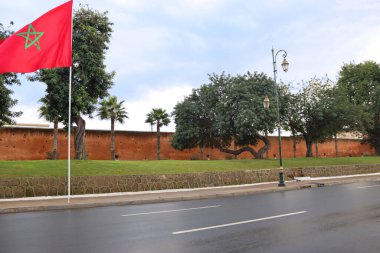 The national flag of Morocco in center of Rabat, capital of Morocco. Historic old wall with trees in the background. clipart