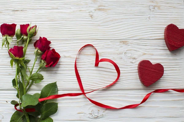 Kırmızı kurdeleli kırmızı güller ve beyaz ahşap arka planda iki tahta kalp.