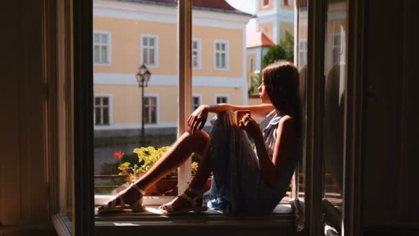 Young girl sitting on window and dreaming. — Stock Video