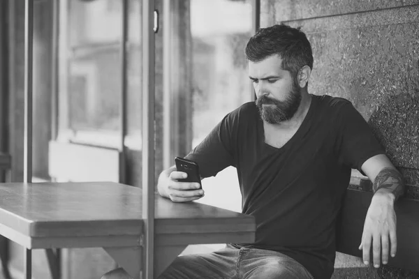 Бородатий чоловік з мобільним телефоном сидить у відкритому кафе — стокове фото