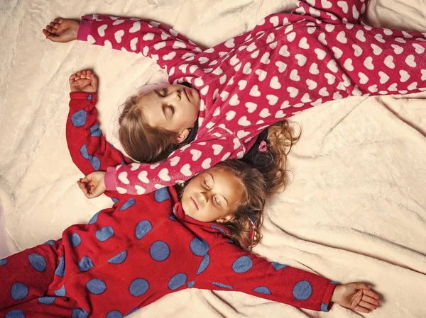 Girls in pajamas sleep in bed, top view