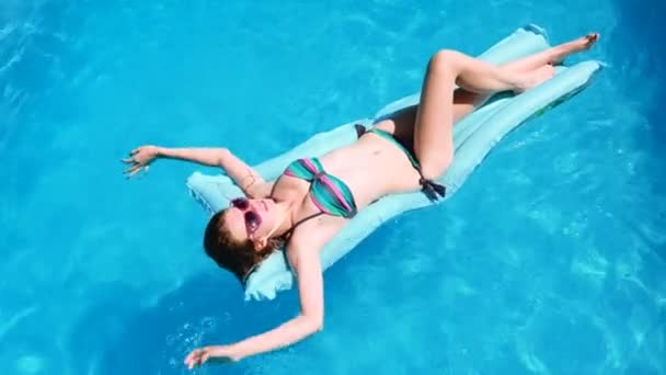 Chica milenaria flotar en la piscina, festival, hotel, playa, evento sonriendo con gafas de sol en verano. Disfrutando del bronceado. Concepto de vacaciones. Vista superior de la mujer joven delgada en bikini en el aire azul — Vídeo de stock
