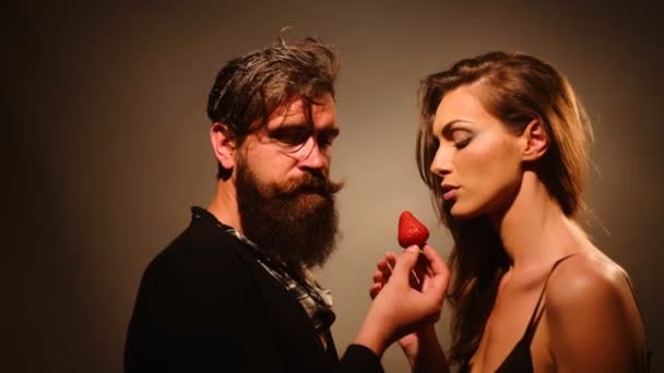 Jovem casal sexy de mulher com rosto bonito e cabelo morena com ombros nus e homem barbudo bonito com barba longa comendo frutas vermelhas de morango — Vídeo de Stock