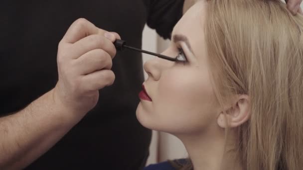 Maquillaje artista aplicar maquillaje a una atractiva mujer joven. Maquillaje para niña. Chica joven en el salón de belleza. Sexy rubia en salón de belleza — Vídeo de stock