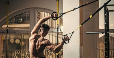 Sporcu, atlet, kas maço mu egzersiz trx döngüler ile arka plan üstünde pencere. Adam çıplak gövde ve geri içinde jimnastik salonu kas eğitim, trx, arka görüş zevk. Spor ve spor salonu konsept