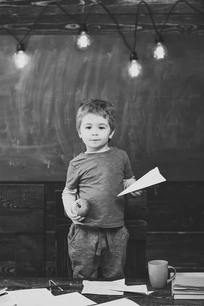 Un niño sosteniendo papel plano y manzana en sus manos. Colegial en camiseta azul de pie detrás de la mesa. Concepto de juego educativo — Foto de Stock