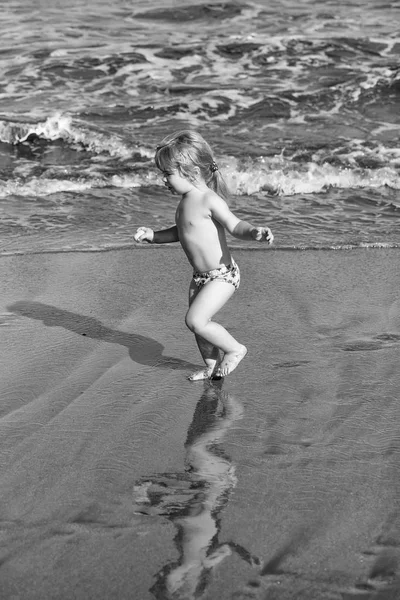 Bonito menino alegre corre na areia molhada ao longo do mar — Fotografia de Stock