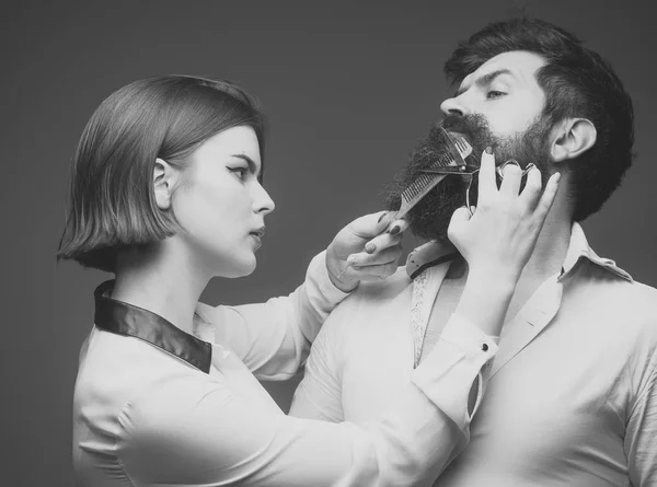 Conceito de barbearia ou cabeleireiro. Cabeleireiro mulher corta barba com tesoura. Cara com penteado moderno visitando cabeleireiro. Homem com barba longa, bigode e cabelo elegante, fundo cinza . — Fotografia de Stock