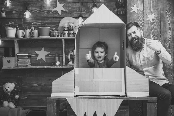 Concepto de lanzamiento de cohetes. Niño feliz sentarse en la mano hizo cohete. Chico jugar con papá, padre, cosmonauta alegre sentarse en cohete hecho de caja de cartón. Niño lindo niño jugar cosmonauta, astronauta, pulgares hacia arriba . —  Fotos de Stock