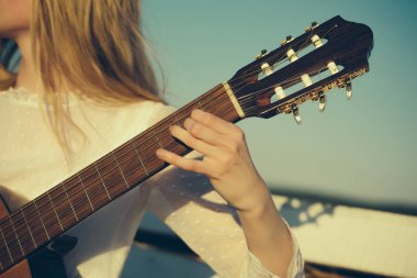 Gitar dizeleri tıngırdatmaya parmak ile. El yaylı çalgılar üzerinde oynamak. Klasik gitar boyun fretboard ve güneşli mavi gökyüzü üzerinde sap kafası. Müzik ve eğlence kavramı.