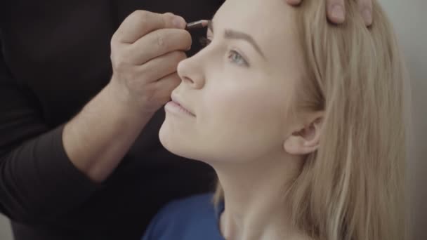 Make-up make-up artiest toepassen op een aantrekkelijke jonge vrouw. Make-up voor het meisje. Jong meisje in de schoonheidssalon. Sexy blond in schoonheidssalon — Stockvideo