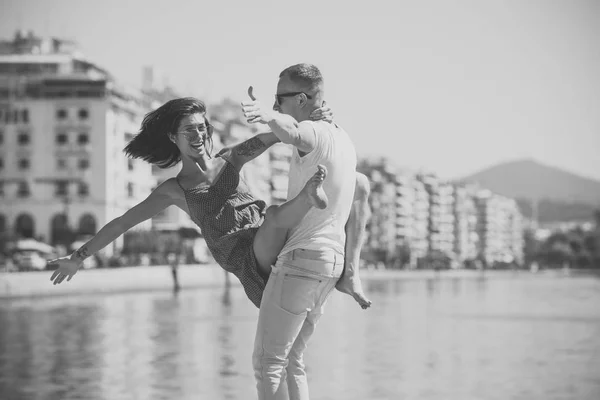 Счастливая семья проводит время вместе, танцуя, веселясь, на морском и городском фоне. Влюбленная пара стоит на берегу. Семейный отдых. Мужчина носит женщину, пара на улыбающихся лицах. Понятие любви — стоковое фото
