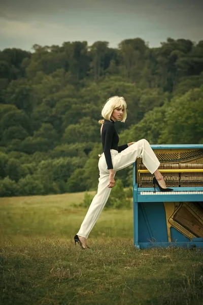 Jovem mulher em peruca loira tocando piano em estilo retro interior com perna no sapato . — Fotografia de Stock