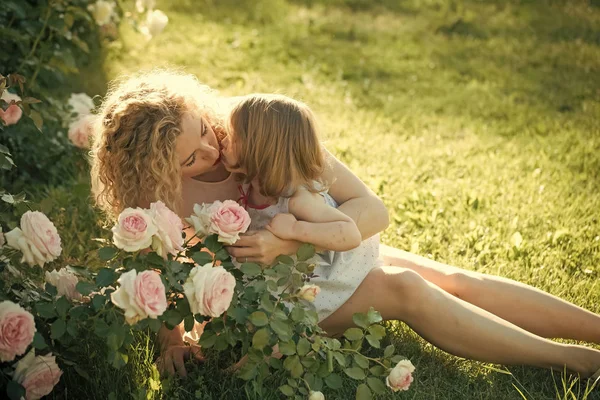 Mamma baciare figlia su erba verde in soleggiata giornata estiva — Foto Stock
