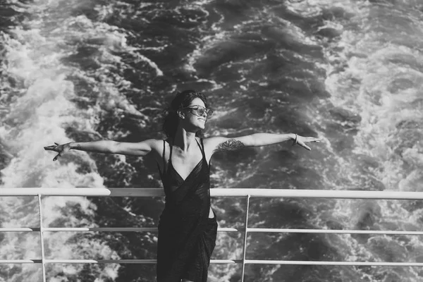 Attractive girl feels free and enjoy summer vacation. Freedom concept. Sexy lady stands on deck of cruise liner with sea waves on background. Woman in dress travelling on cruise ship on sunny day