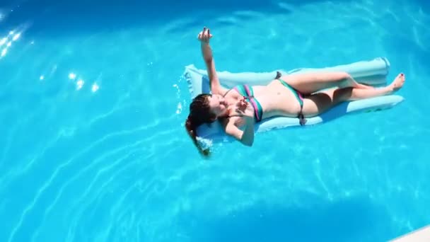 Millennial menina flutuar na piscina, festival, hotel, praia, evento sorrindo com óculos de sol durante o verão. A desfrutar do bronzeado do sol. Conceito de férias. Visão superior da jovem mulher magra em biquíni no ar azul — Vídeo de Stock