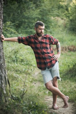 Bearded man standing on path. Hipster hiking in woods. Benefits of walking barefoot. Health and fitness concept. clipart