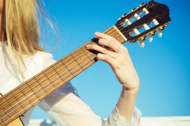 Klasik gitar boyun fretboard ve güneşli mavi gökyüzü üzerinde sap kafası. Gitar dizeleri tıngırdatmaya parmak ile. El yaylı çalgılar üzerinde oynamak. Müzik ve eğlence kavramı.