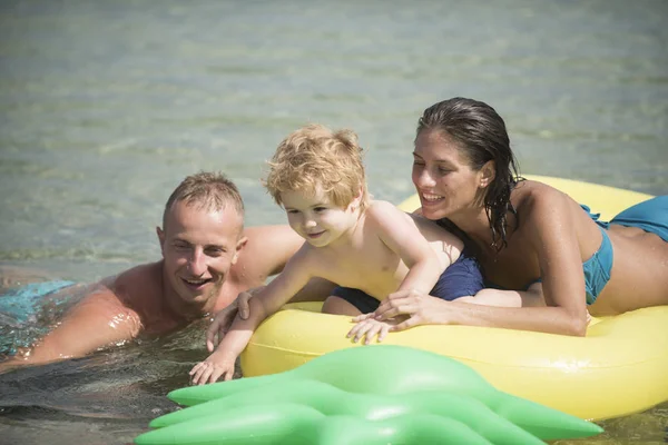 父とマットレスに近い母は 息子と一緒に泳ぐ 家族は 一緒に時間を過ごす楽しんでいます エアマットレス パイナップル両親と海の形をしたかわいい子少年が座っています 家族での休暇の概念 — ストック写真