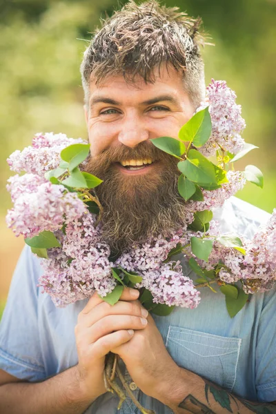 在花园里拿着丁香的大胡子男子 园丁用胡须捧着紫色的花朵 春天的概念 人与胡子愉快的面孔享用花的芳香 时髦的胡子和纹身在公园散步 — 图库照片
