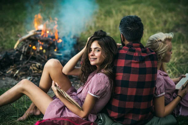 森の中でピクニックを持つ友人 人の女の子に彼に傾くキャンプファイヤーを見て元に戻す 本を読んで中かっこでブルネットの少女の笑顔 — ストック写真