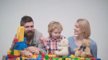 Genç aile inşaat plastik blokları ile oyun oynamak. Aile Oyunları kavramı. Anne ve çocuk mutlu yüzler ile kırmızı tuğla tutun. Baba, anne ve oğlu ışık ahşap arka plan üzerinde oyun odası