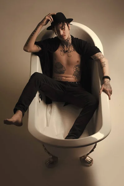 Hombre con sombrero negro y ropa acostado en la pestaña del baño —  Fotos de Stock
