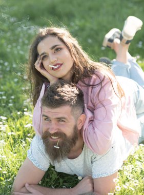 Mutlu çift yalan yeşil çayır çimen. Sakallı adam kız açık havada, bahar zaman kavramı ile güneşli gün zevk. Gülümseyen adam papatya veya papatya ve seksi kız ağzına sigara ile çiğneme.