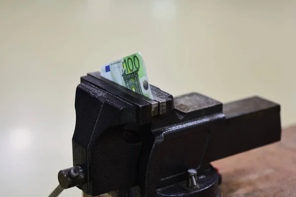 Vise tool fix paper money on workbench. Hundred euro banknote squeezed in vise. Euro currency devaluation or inflation and default. Finance and banking crisis. Economy and business problem.