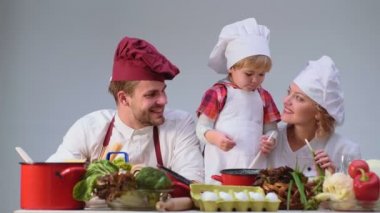 Sevimli küçük bir çocuk ve onun güzel anne mutfakta yemek yaparken gülümsüyorsun. Genç aile yemek yemek mutfakta. Mutlu bir aile birlikte yemek. Mutlu genç ailesi ile anne, baba çocuk yemek.