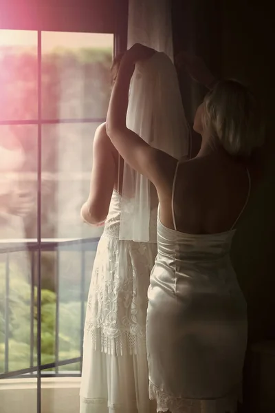 Hübsche Brautjungfer hilft schöne Braut, Schleier anzuziehen — Stockfoto
