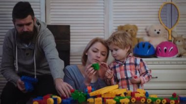 Genç aile inşaat plastik blokları ile oyun oynamak. Aile Oyunları kavramı. Anne ve çocuk mutlu yüzler ile kırmızı tuğla tutun. Baba, anne ve oğlu ışık ahşap arka plan üzerinde oyun odası.