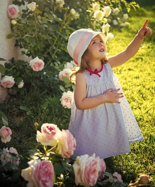 Щаслива дитина розважається. Дівчина в капелюсі вказує пальцем в літньому саду — стокове фото