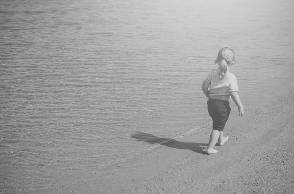 Chico feliz divirtiéndose. Niño en camiseta y pantalones cortos caminar en la playa tropical — Foto de Stock