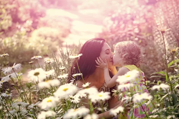 Chico feliz divirtiéndose. Hija beso madre en soleado floral paisaje —  Fotos de Stock