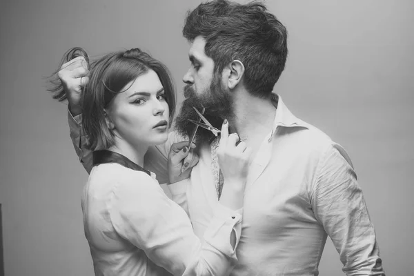 Guy avec coiffure moderne visitant coiffeur. Concept coiffeur ou salon de coiffure. Homme à longue barbe, moustache et cheveux élégants, fond clair. Femme coiffeur coupe barbe avec des ciseaux . — Photo