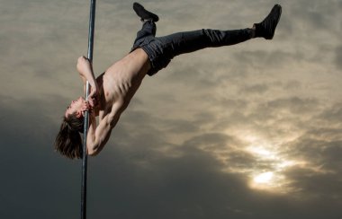 Güçlü adam dansçı egzersiz günbatımı kutbunda üzerinde. Seksi maço erkek sinek. Pilon üzerinde dans kas delikanlı. Atletik adam pilon üzerinde akrobatik öğeleri olun. Pole dans spor. Yolda büyük bir şekle