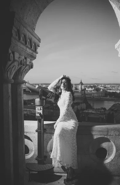 Schönheitsmodenporträt. Frau mit Teleskop am Aussichtspunkt auf das Stadtbild. Sinnliche Frau mit langen Haaren im weißen Hochzeitskleid, Mode. Mädchen mit Glamour-Look und Make-up, Schönheit. Modelreise — Stockfoto