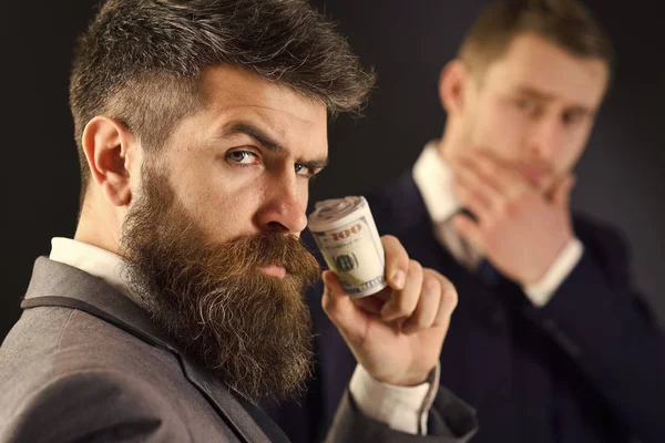 Un homme élégant en costume. L'homme au visage sérieux tient le rouleau fait de dollar, d'argent, paie au partenaire. Concept de partage des bénéfices. Rencontre d'hommes d'affaires réputés, fond noir — Photo