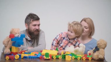 Genç aile inşaat plastik blokları ile oyun oynamak. Aile Oyunları kavramı. Anne ve çocuk mutlu yüzler ile kırmızı tuğla tutun. Baba, anne ve oğlu ışık ahşap arka plan üzerinde oyun odası