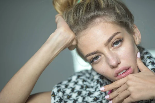 Tired woman with sleepy look holding her head. Girl with hair in messy knot in black and white outfit isolated on gray background. Mood swings, depression, emotional problems concept.