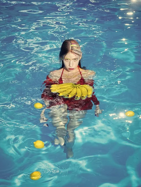 Modelo de mulher de moda posando. Vitamina em banana em menina que se senta perto de água. mulher com frutas tropicais na piscina. Mulher relaxar na piscina spa. Férias de verão e viagens ao oceano. Alimentação e saudável orgânica — Fotografia de Stock