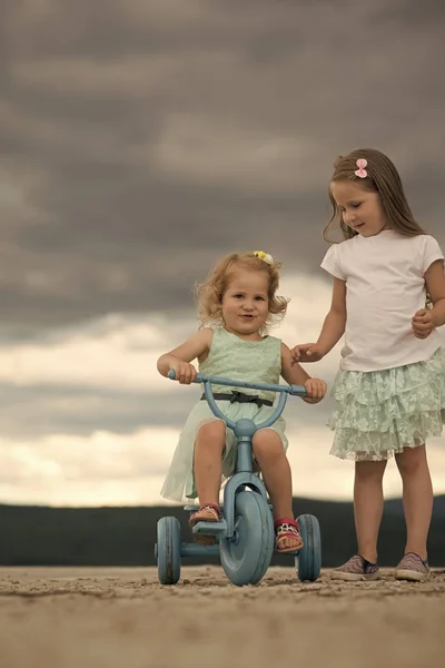 Kind Kindheit Kinder Glückskonzept. Mädchen fährt Dreirad mit Schwester bei bewölktem Himmel — Stockfoto