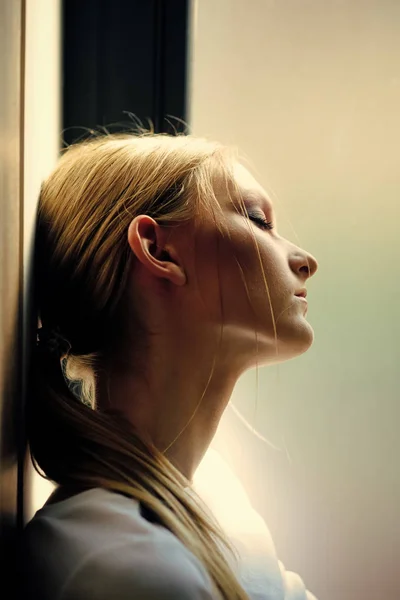 Secretos para mujeres. Mujer con pelo rubio cola de caballo relajarse en la ventana, ensueño. Sueño, ensueño, meditación. Bienestar y relax de la joven. Mujer belleza y moda. retrato de perfil de chica reflexivo —  Fotos de Stock